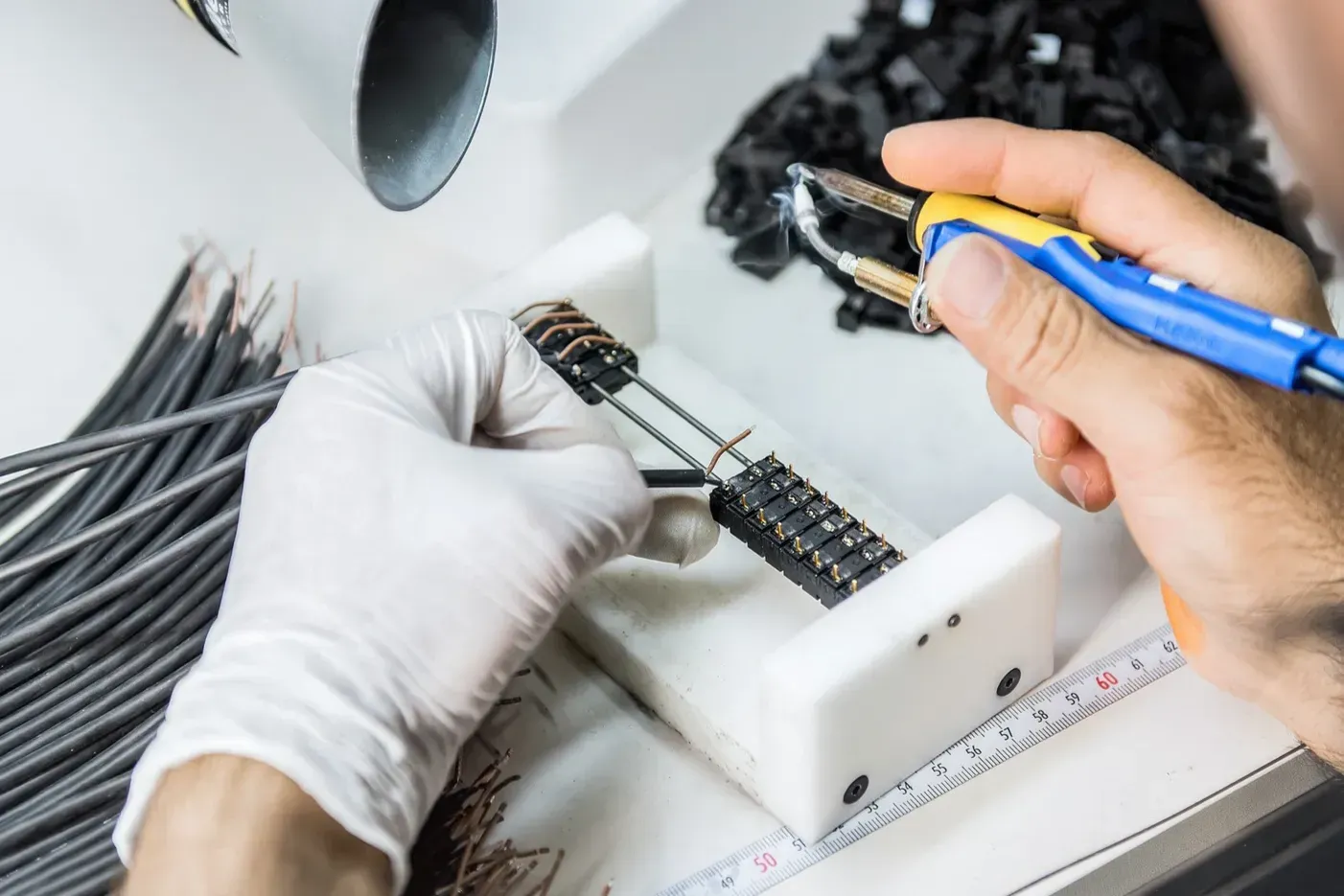 Techniker lötet Steckverbinder für die elektronische Serienfertigung in der Logistik – präzise Handarbeit mit Lötkolben und Schutzhandschuhen
